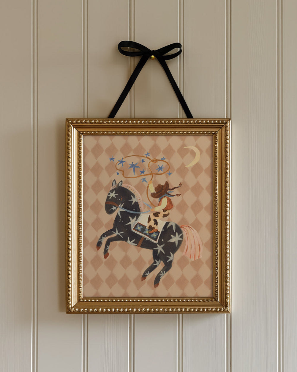 Framed artwork of a cowgirl riding a horse with a decorative pattern on a wall.
