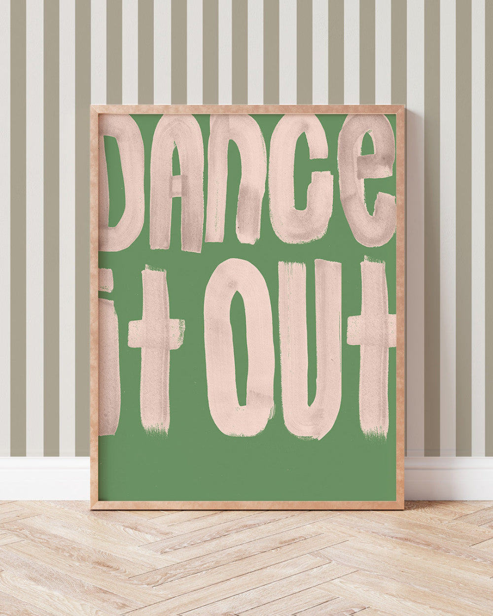 Framed artwork with 'Dance It Out' text on a green background, placed on a wooden floor with striped wallpaper.