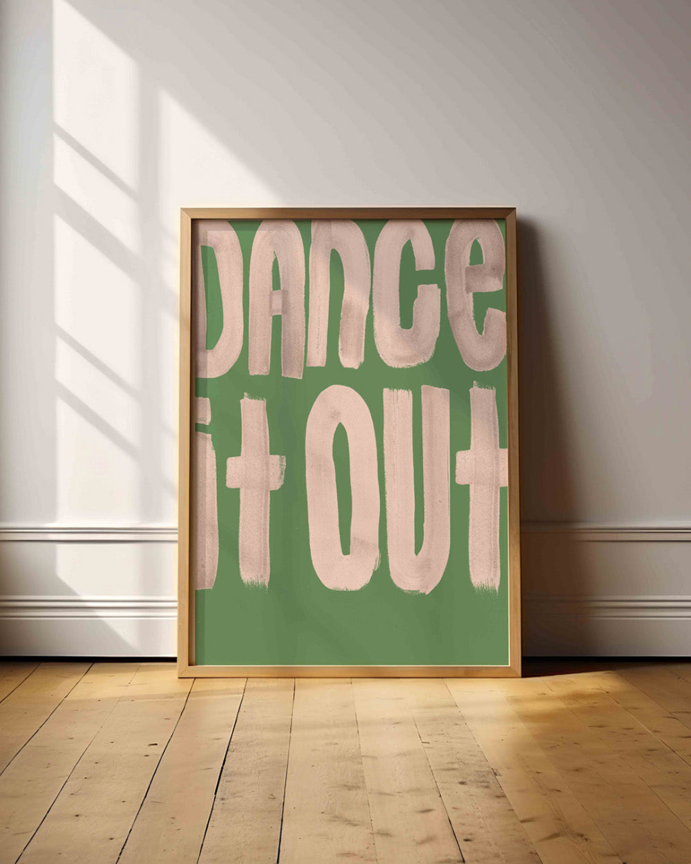 Framed poster with 'Dance It Out' text on a green background in a room with wooden floor and white walls.