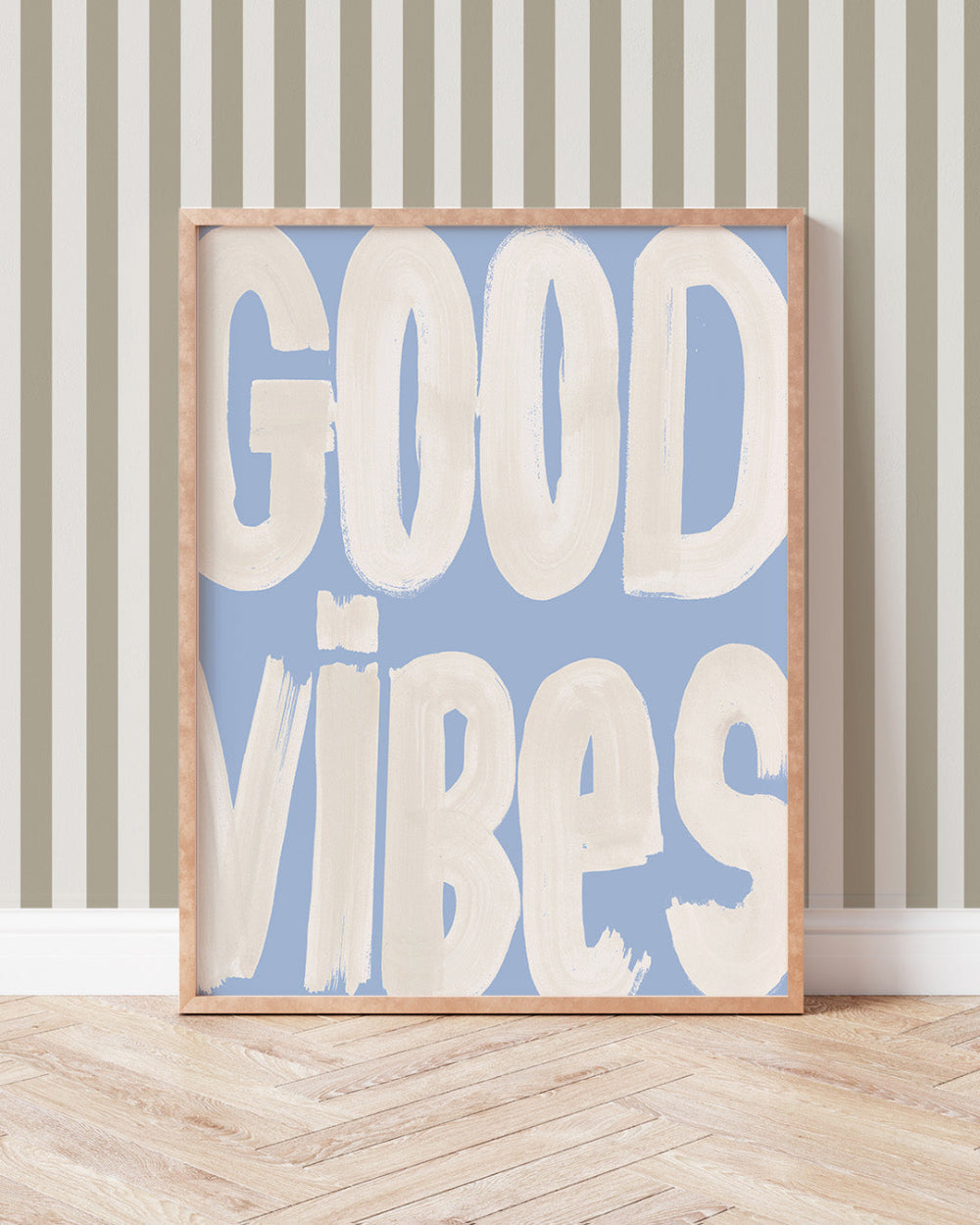 Framed artwork with 'GOOD VIBES' text on a blue background, leaning against a striped wall.