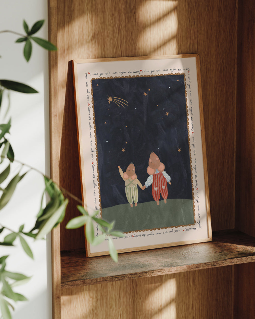 Framed artwork of two mice holding hands under a starry sky on a wooden shelf. 'I need you more than anything darling' quote.