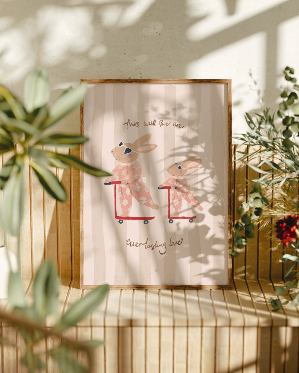 Framed artwork with two rabbits on scooters in a natural setting with plants.