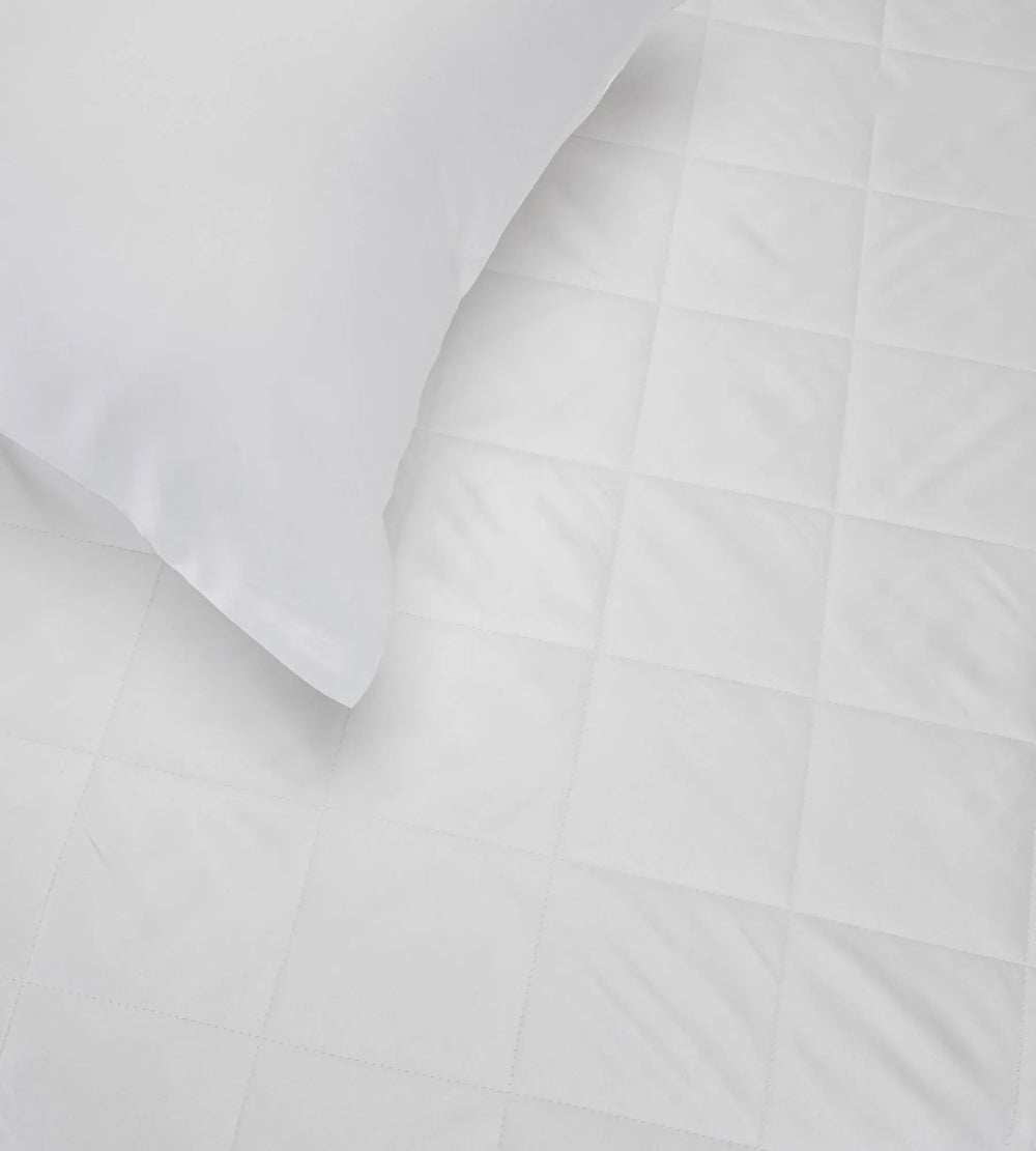 Close-up of a white bamboo pillow with a bamboo mattress protector details on a light grey background