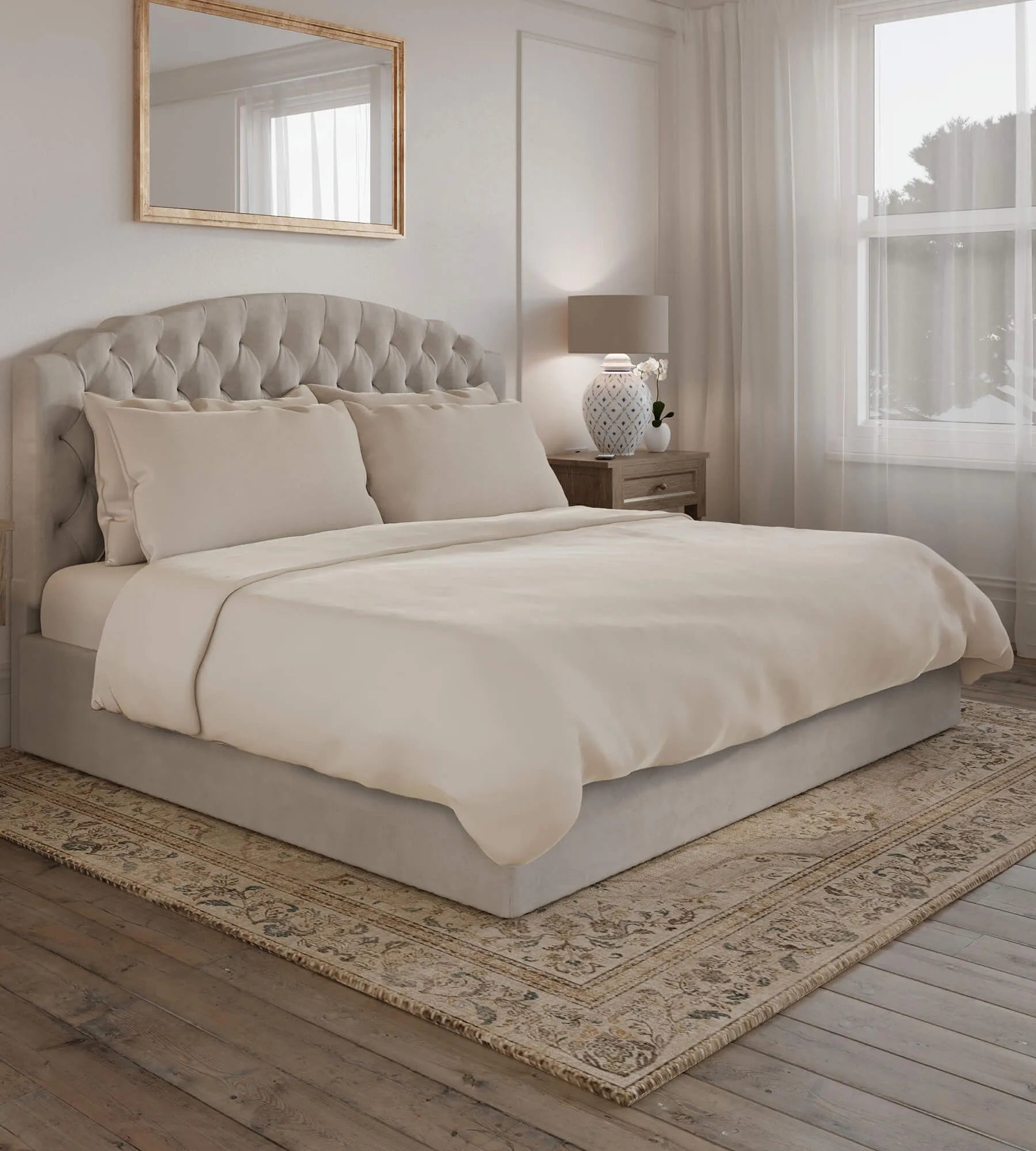 Neatly made bed in a bedroom with a mirror and lamp in the background.