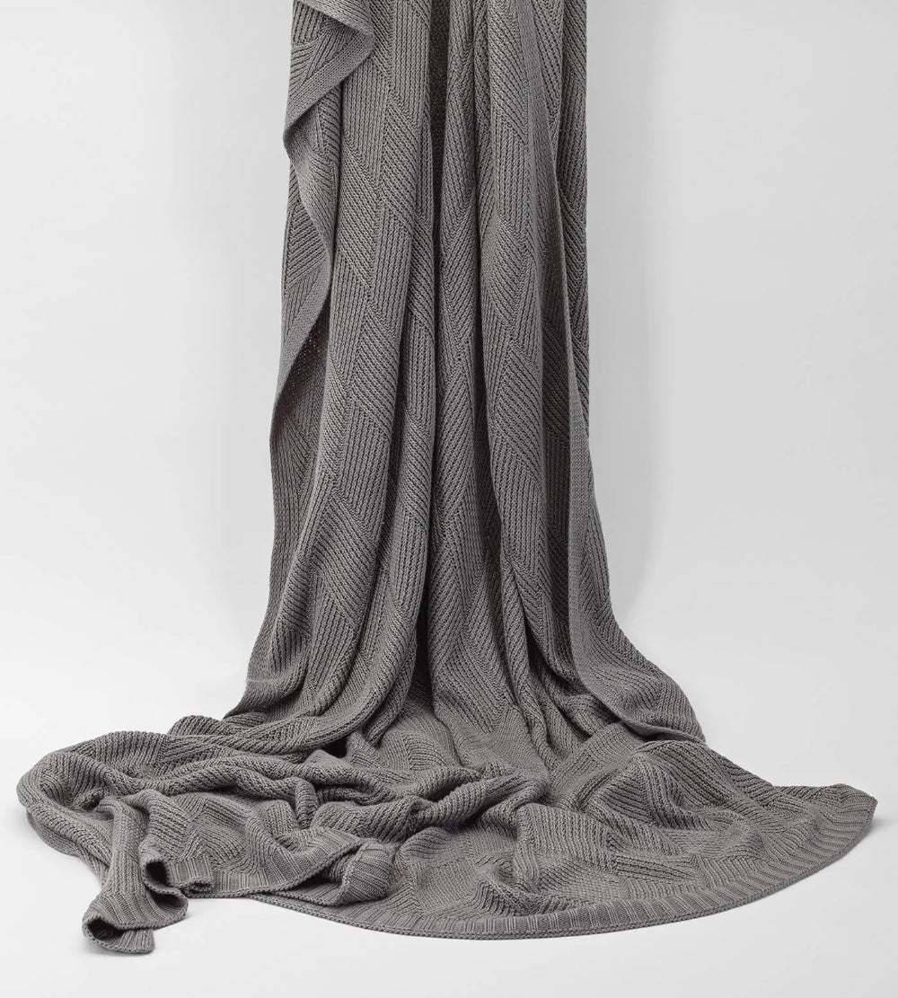Grey knitted blanket draped over a white surface