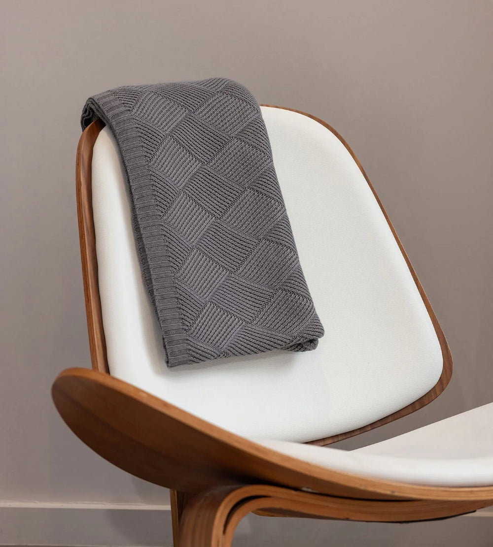 Gray textured blanket draped over a white chair with wooden frame against a plain background
