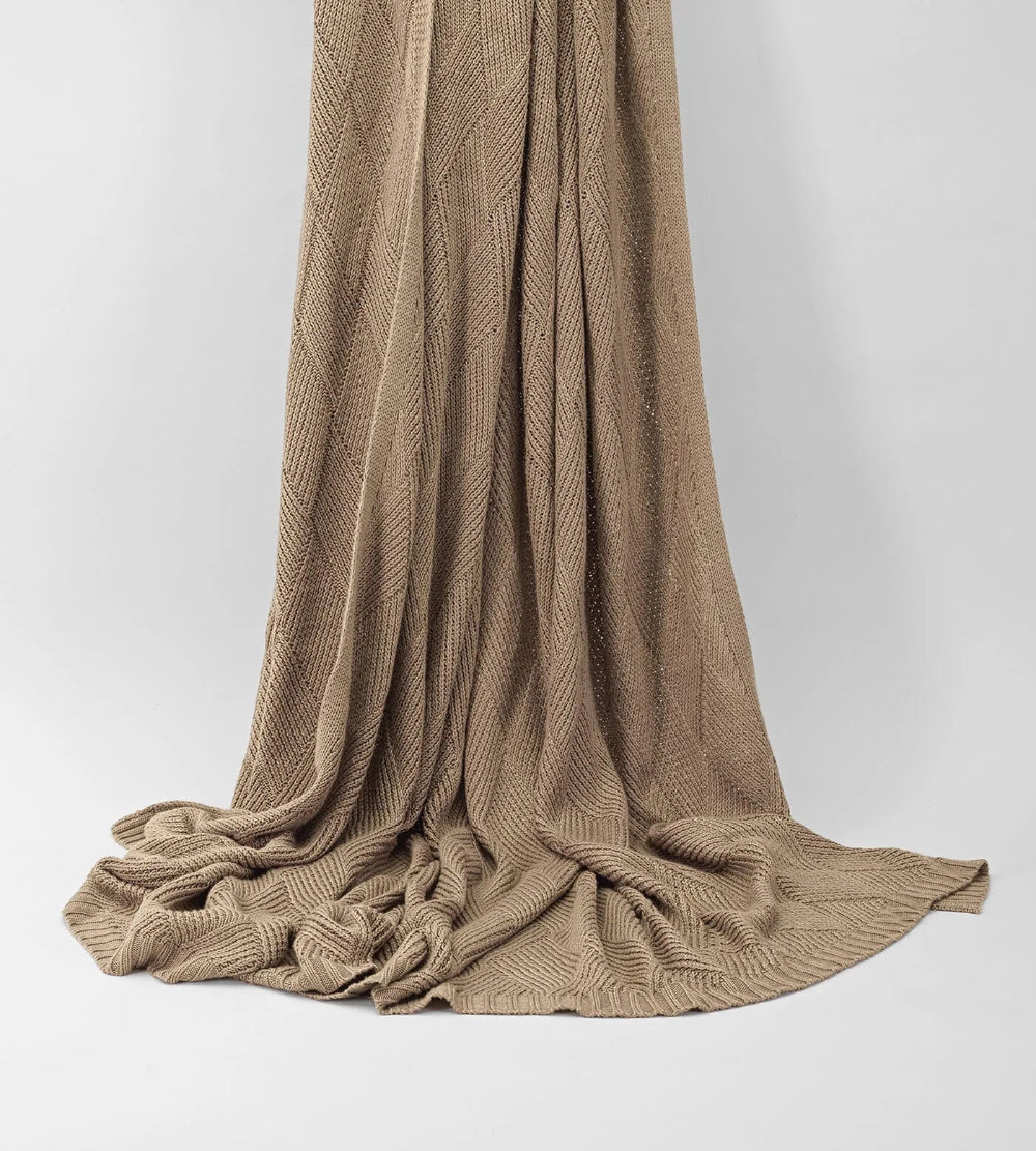 Brown knitted blanket draped over a white background