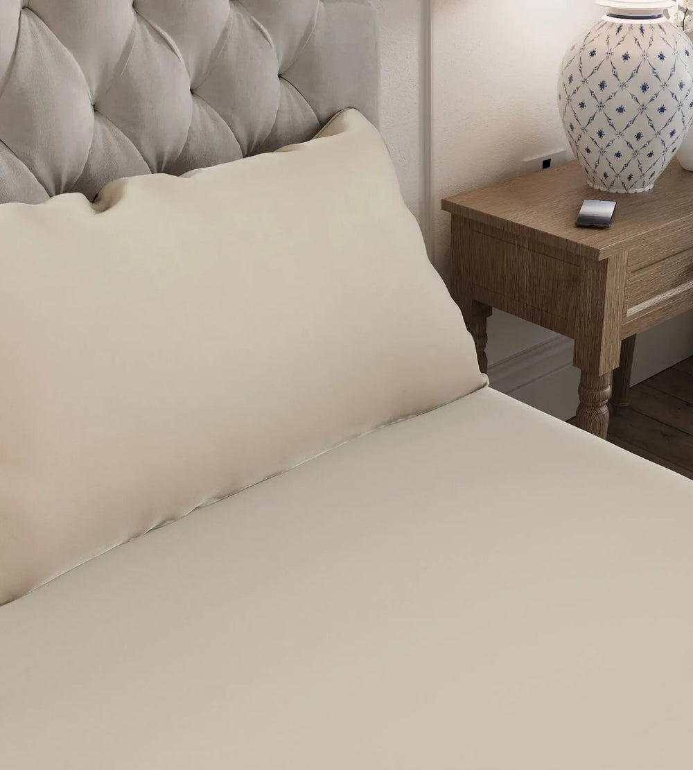 Oatmeal bedspread on a bed with a wooden nightstand and decorative lamp in the background.