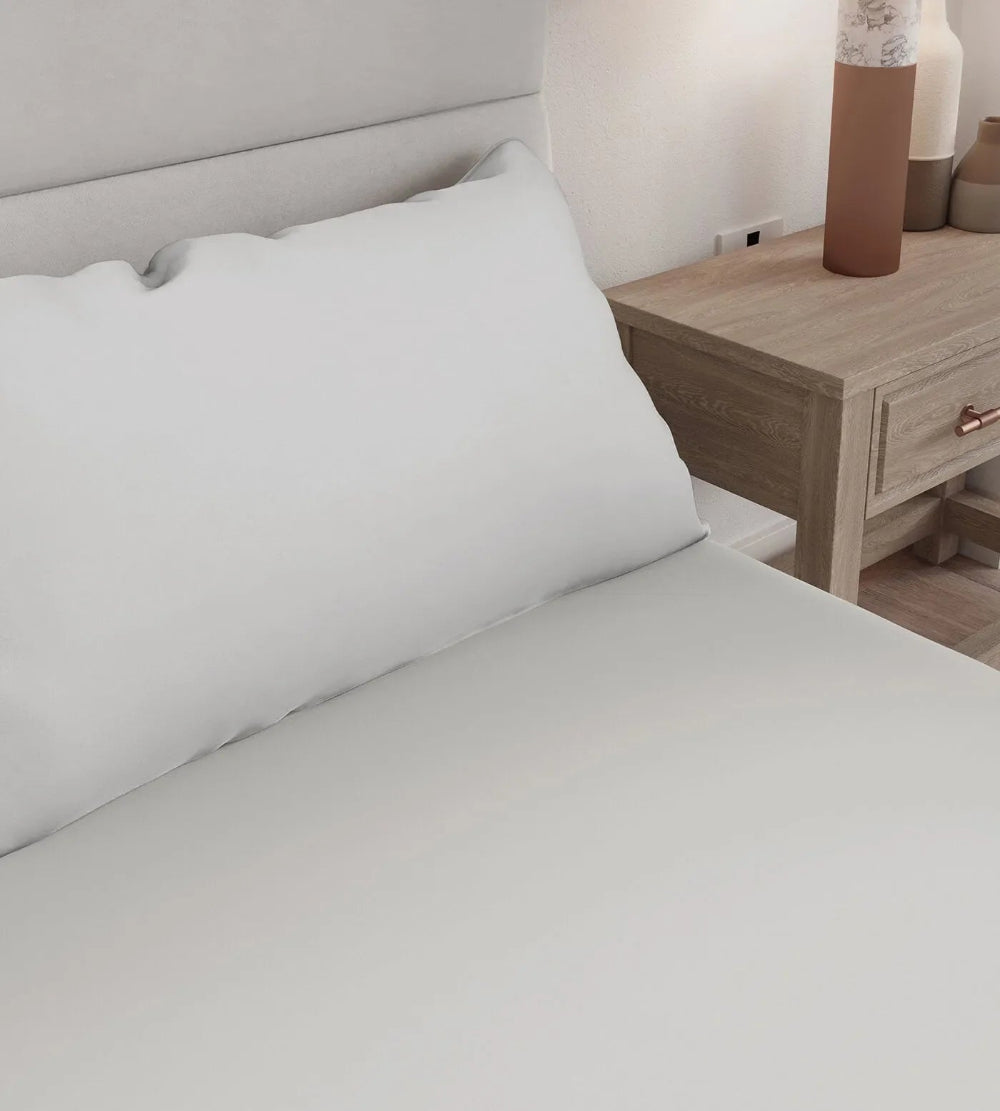 White bedding on a bed with a wooden nightstand in the background