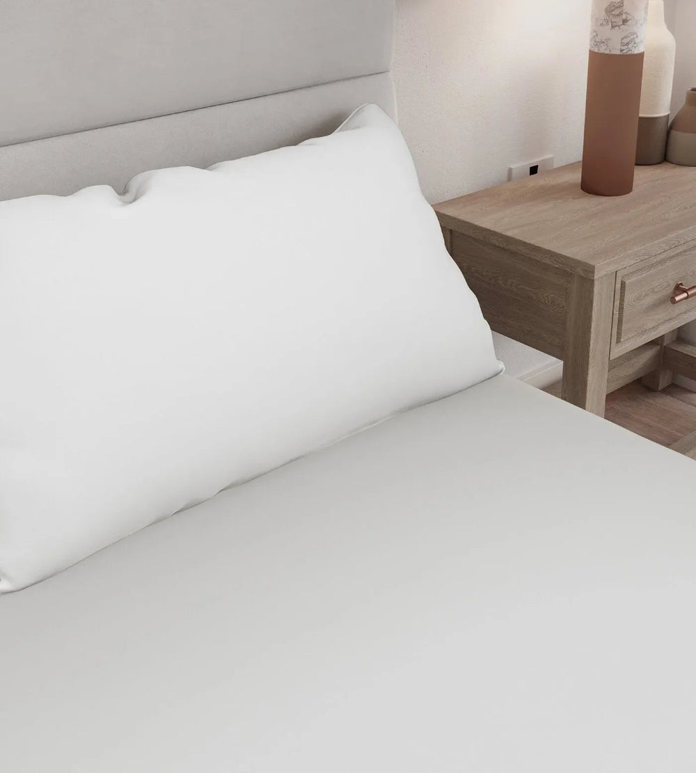 White pillowcases on a bed next to a wooden nightstand with a lamp.