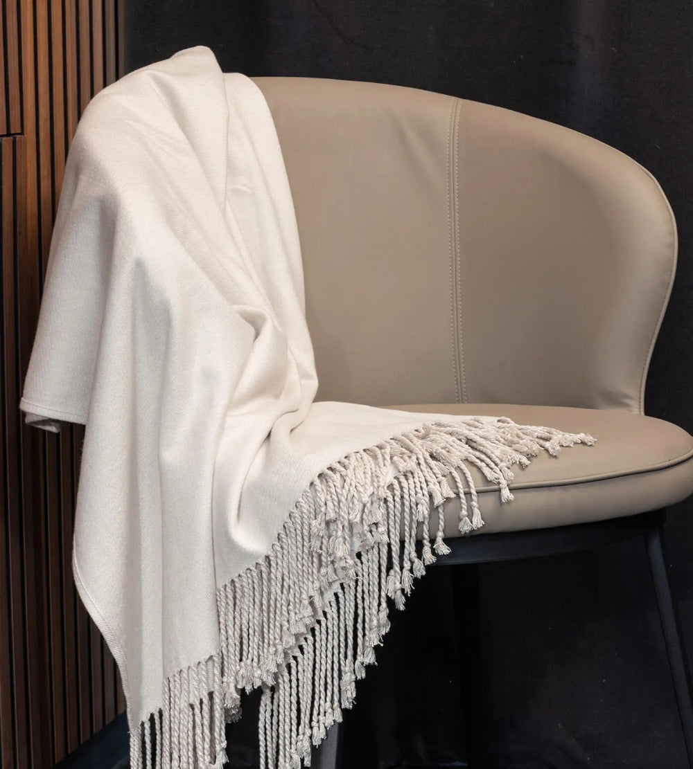 White blanket with fringe draped over a beige chair against a dark background