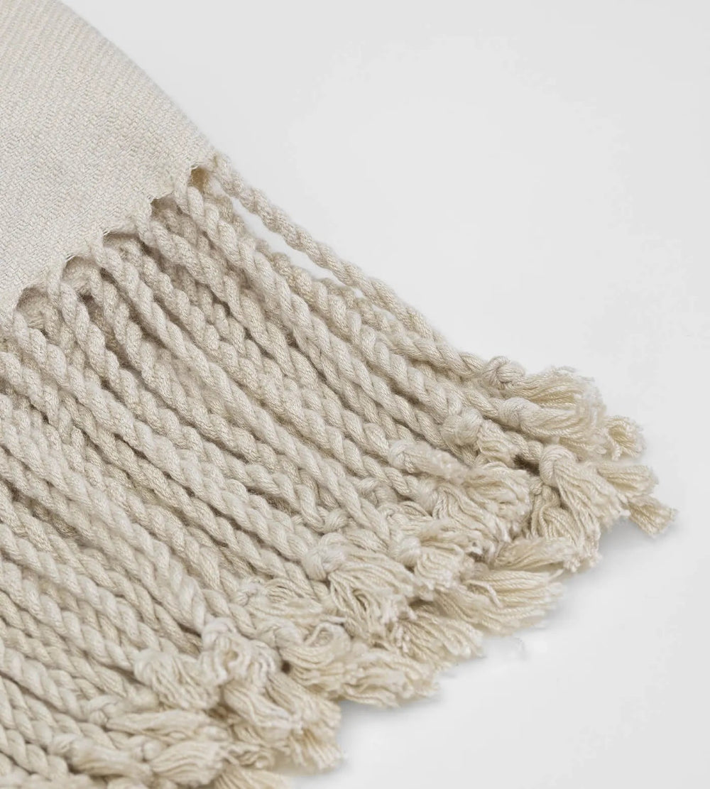 Close-up of a beige woven bag with tassels on a light grey background