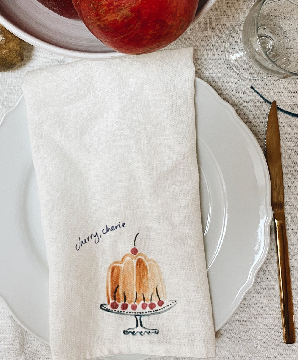 Napkin with cherry-themed design on a table setting with a plate and knife.