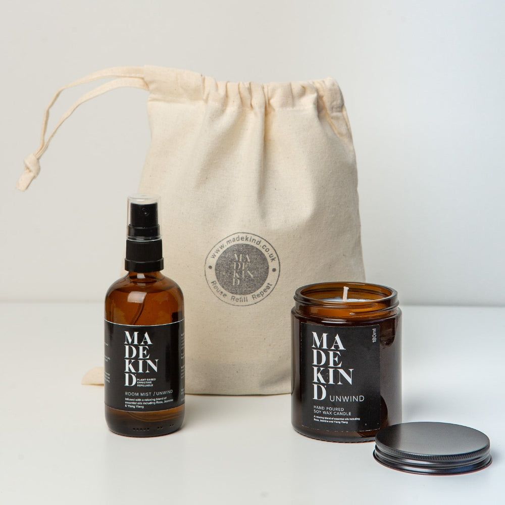 Two amber glass bottles with black labels and a beige drawstring bag on a white background. One Body Mist and One candle called unwind