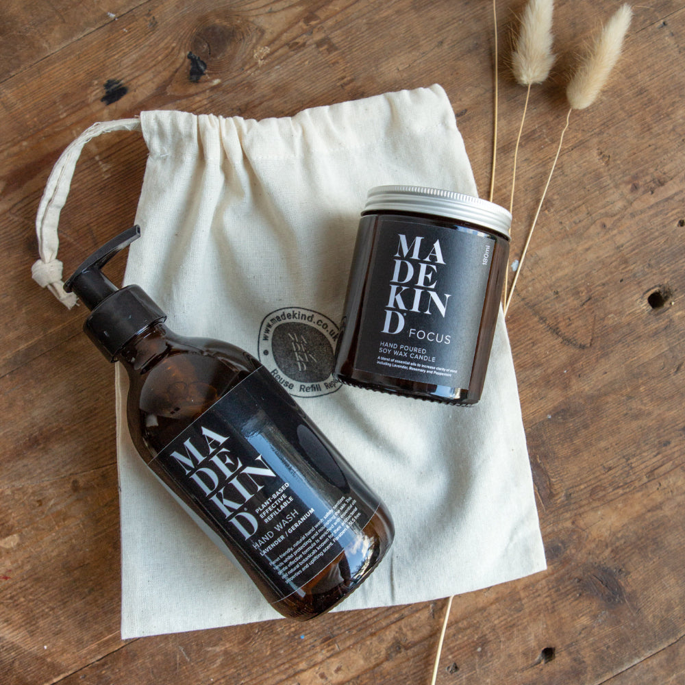 One bottle labelled 'MADE KIND' on a wooden surface with a drawstring bag with a Hand Poured candle called Focus.