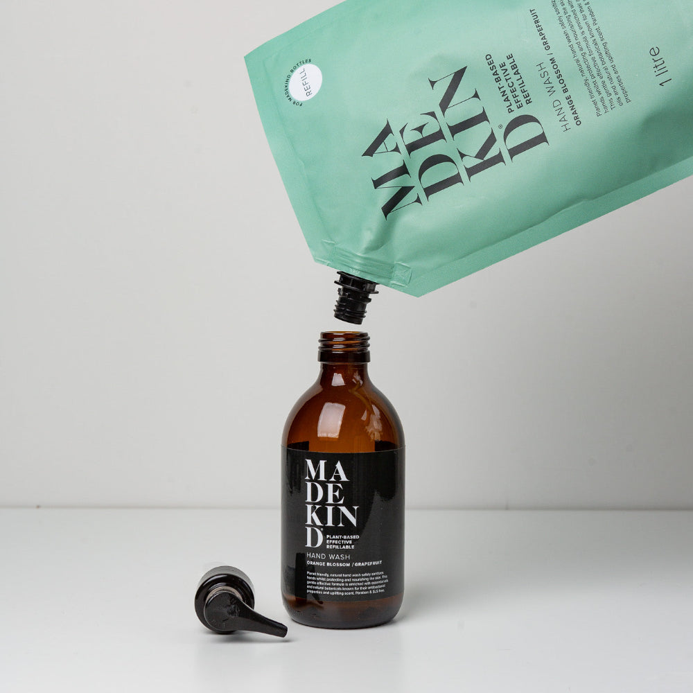 Made kind skincare product being poured from a green pouch into a brown bottle on a white background