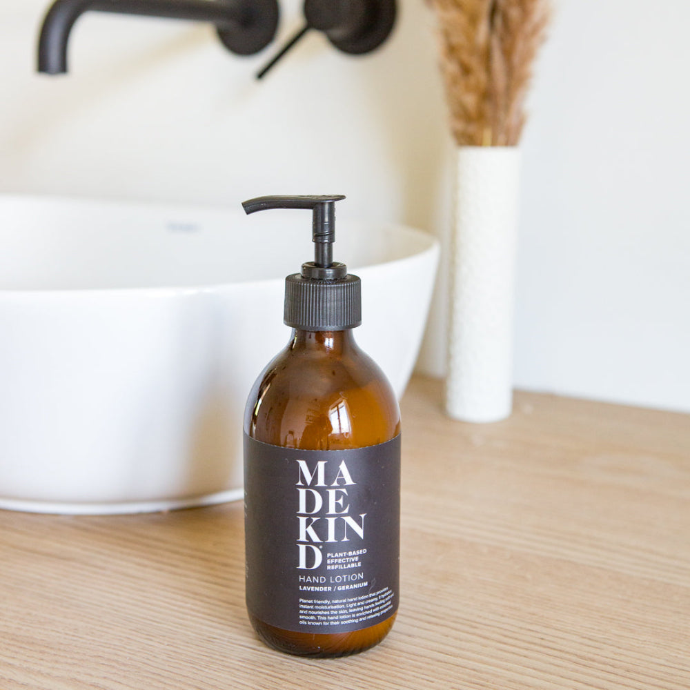 Bottle of Madekind hand lotion on a wooden surface with a blurred bathroom sink background