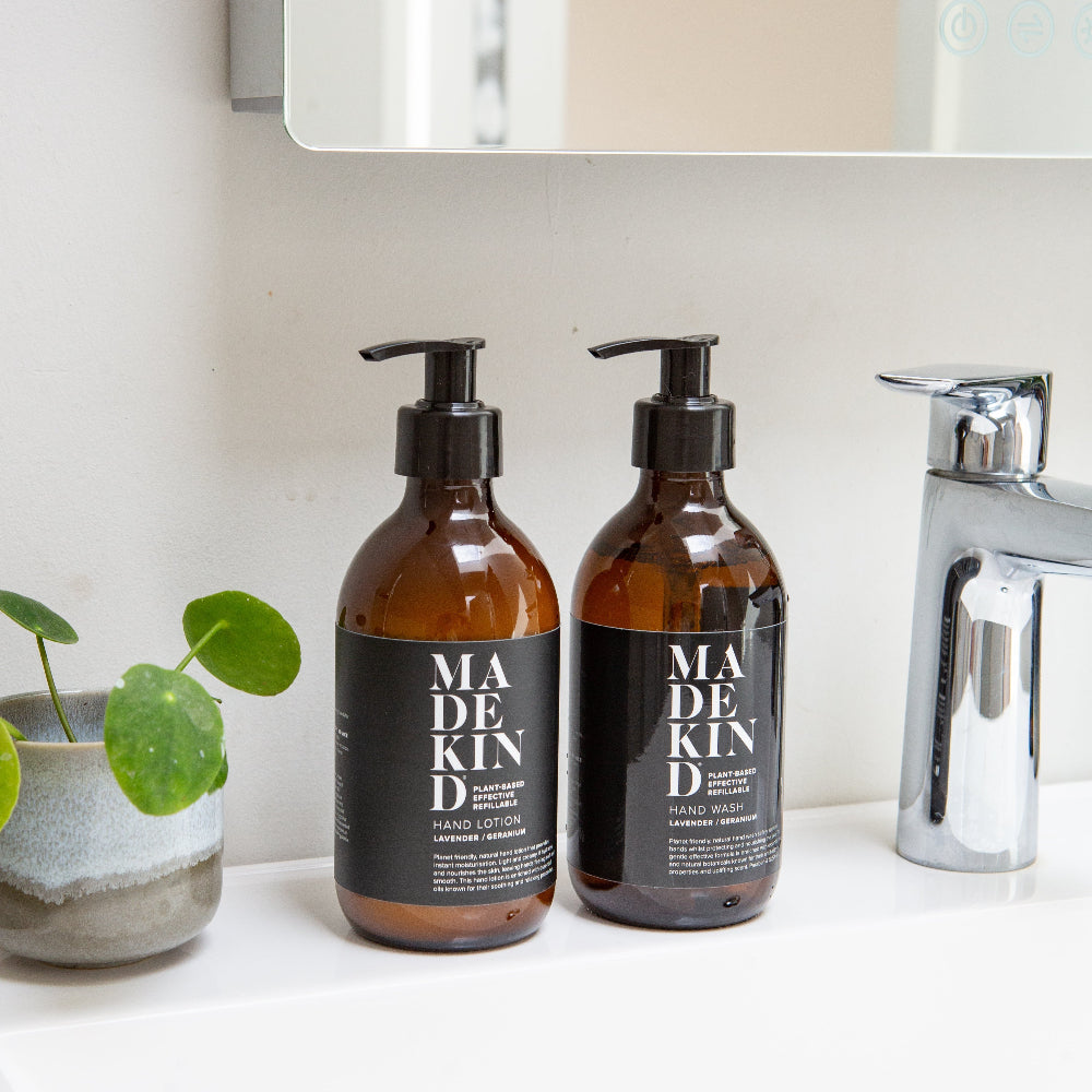 Two bottles of Madekind hand wash and hand lotion on a bathroom counter with a plant and shower head in the background.