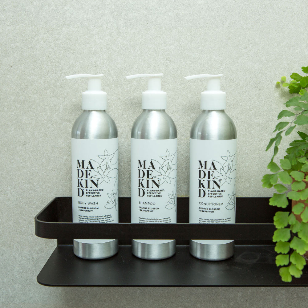 Three bottles of 'MADE KIND' skincare products Shampoo Conditioner and Body Wash on a black tray with a plant in the background.