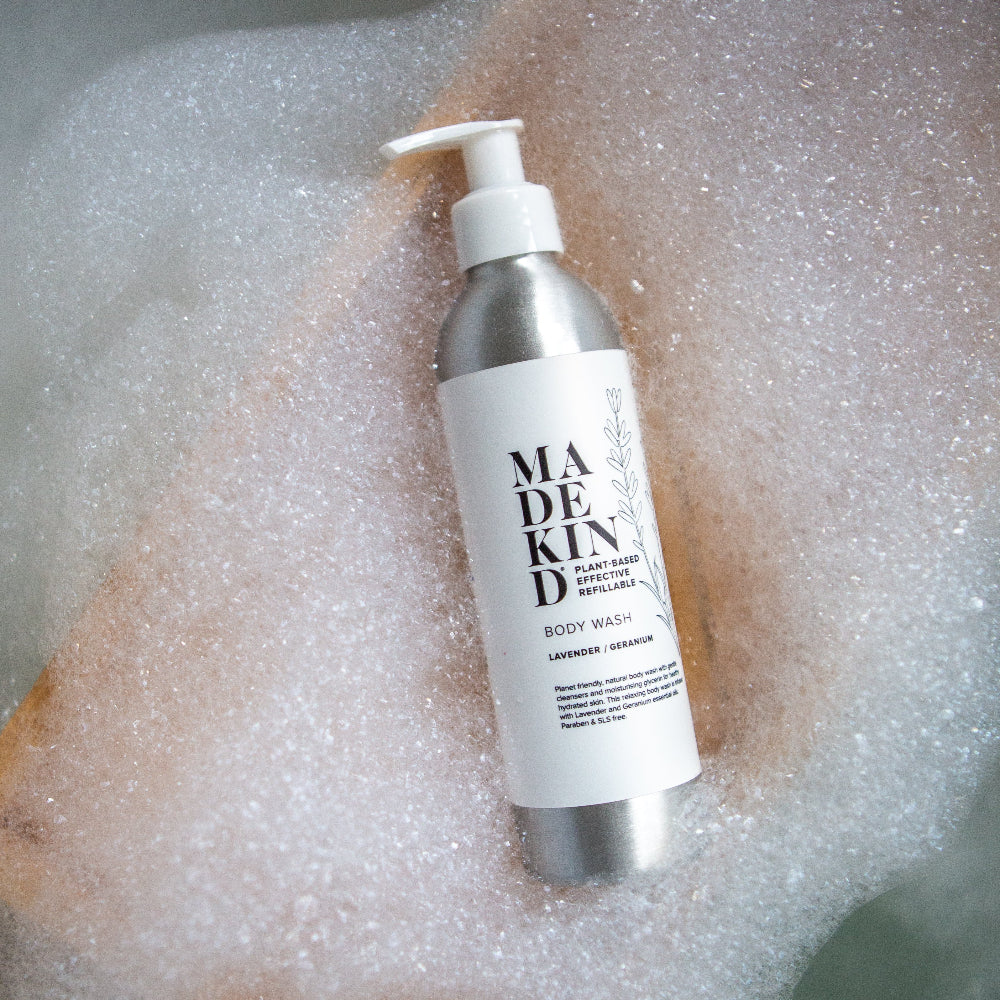 Body wash bottle labeled 'MADEKIND' on a textured surface with bubbles.