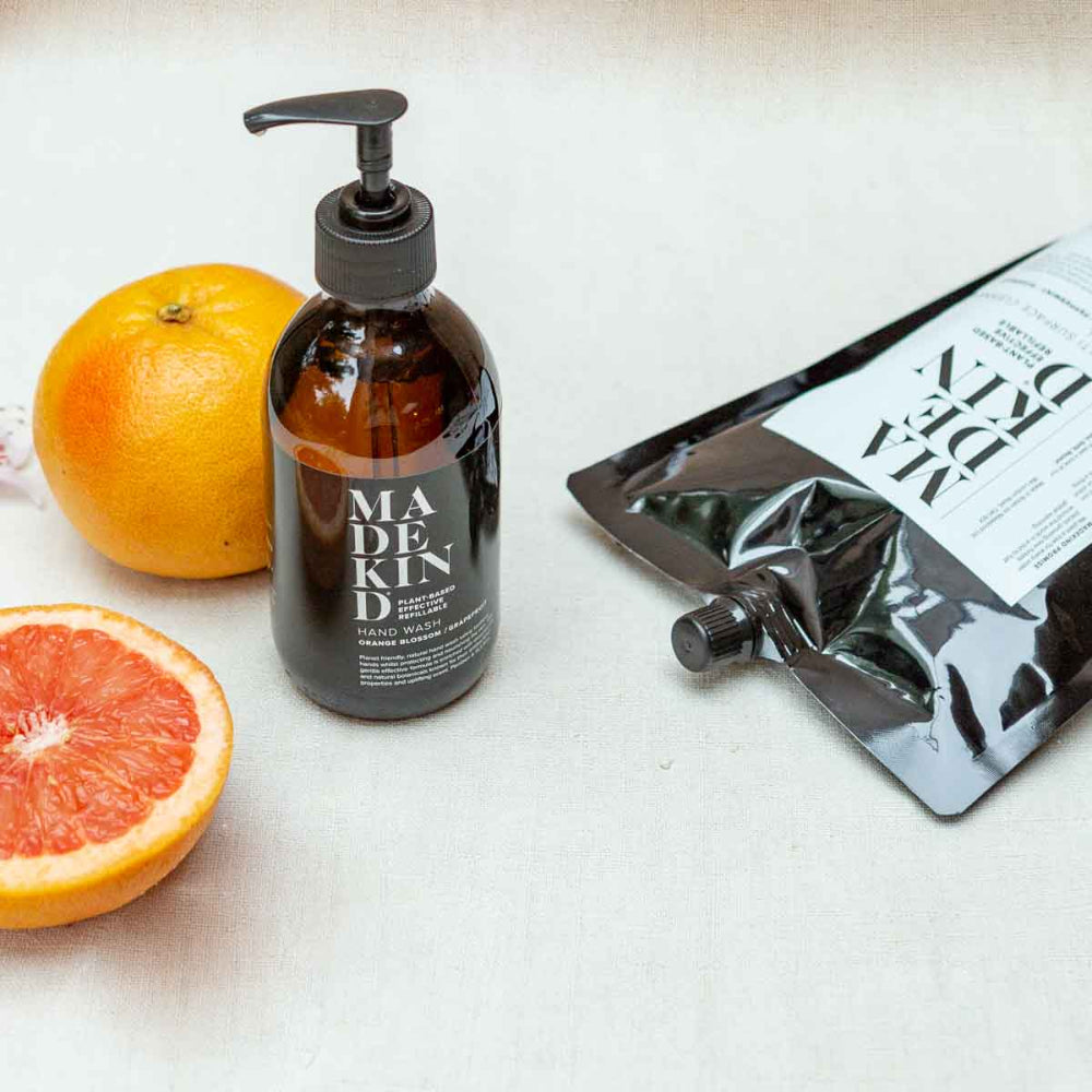 Bottle of 'MADE KIND' Hand wash with a half-cut grapefruit and a black pouch on a white surface