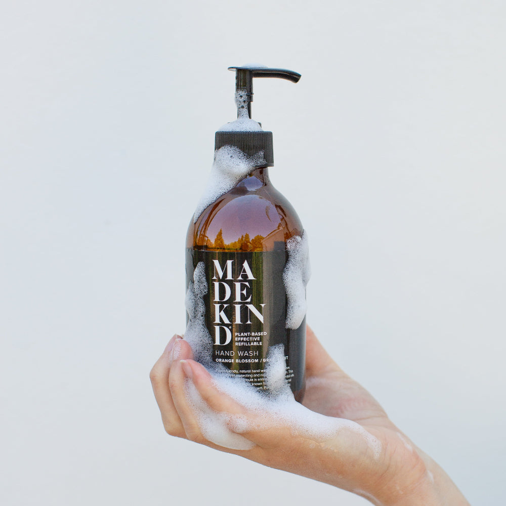 Hand holding a bottle of Made kind hand wash with a white background soap suds dripping down the bottle into palm of hand
