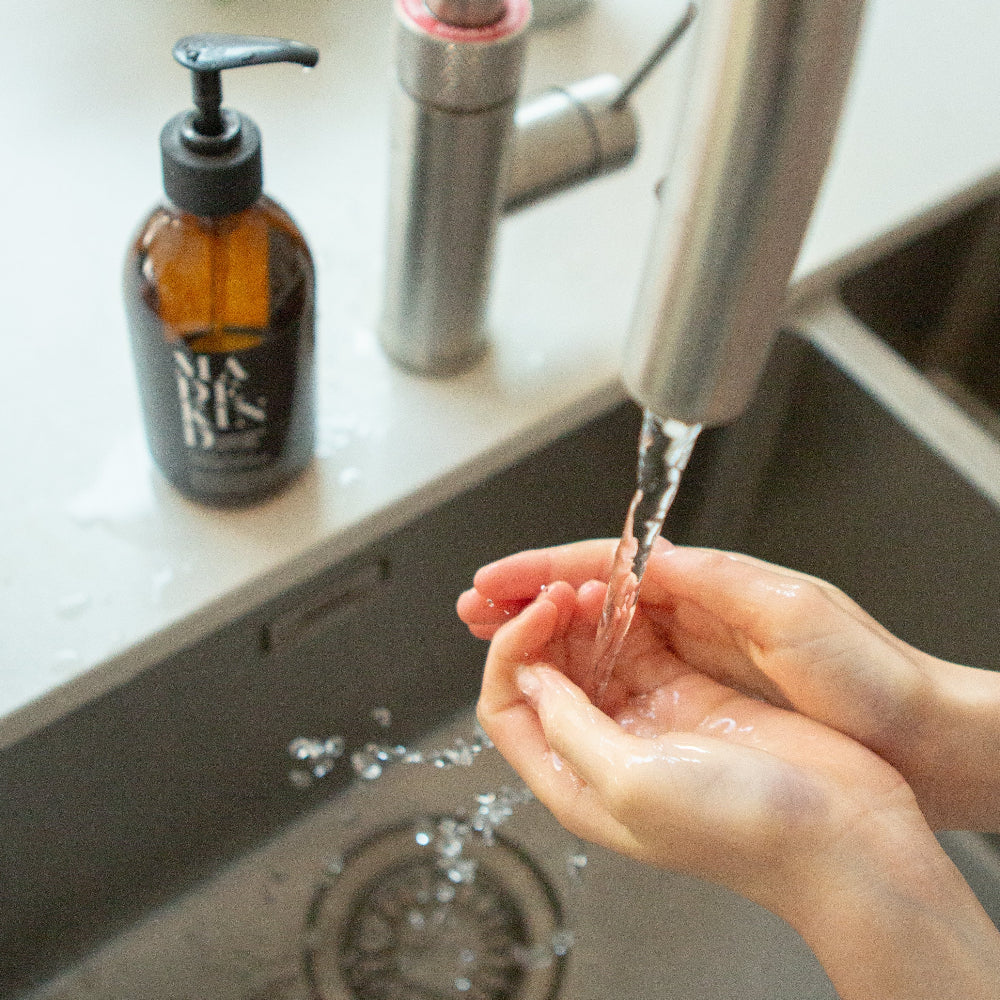 Person washing hands under running water in a kitchen sink with a soap dispenser from Made Kind in the background.