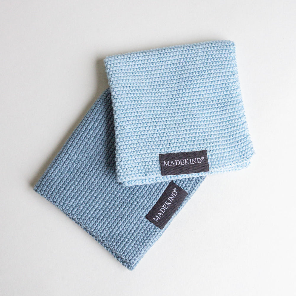 Two light blue knitted dishcloths with 'MADEKIND' labels on a white background