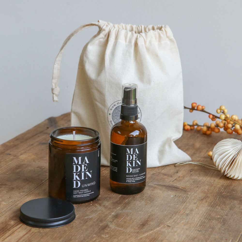 Madekind candle and room mist bottle on a wooden surface with a drawstring bag in the background.