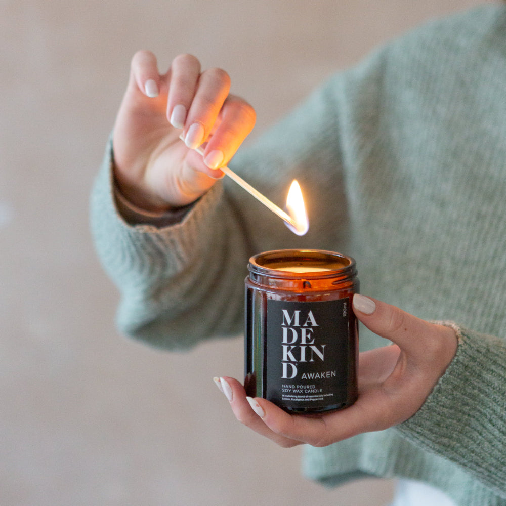 Person lighting a candle labelled 'MADEKIND Awaken' with a match.