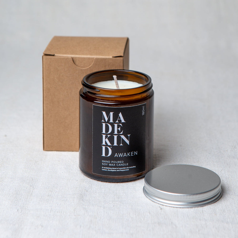 Madekind Candle in an amber jar with a black label, next to a cardboard box on a light grey background