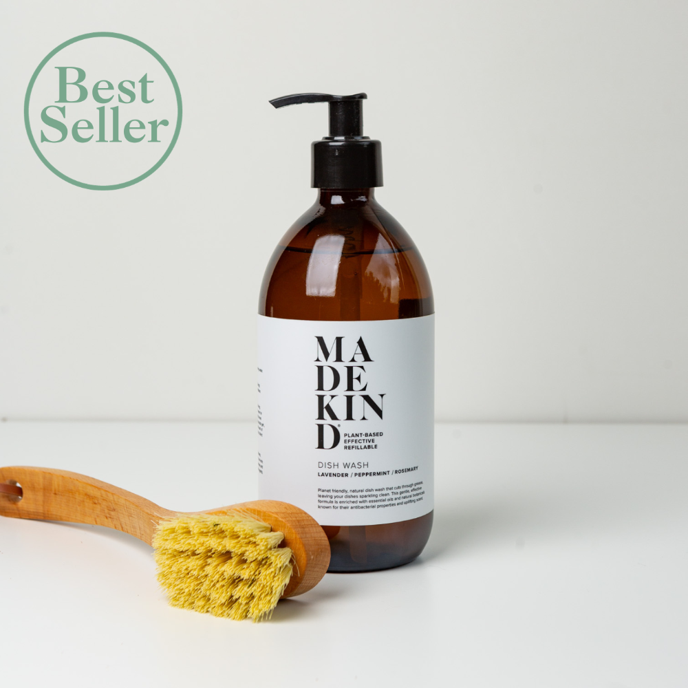 Brown bottle of 'MADEKIND' dish wash with a wooden scrubber on a light background.