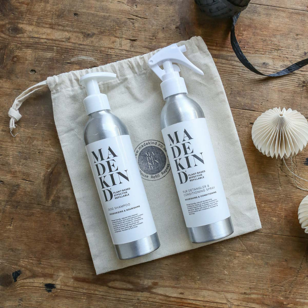 Two bottles Dog grooming shampoo and conditioner of 'MADEKIND' on a beige drawstring bag on a wooden surface.