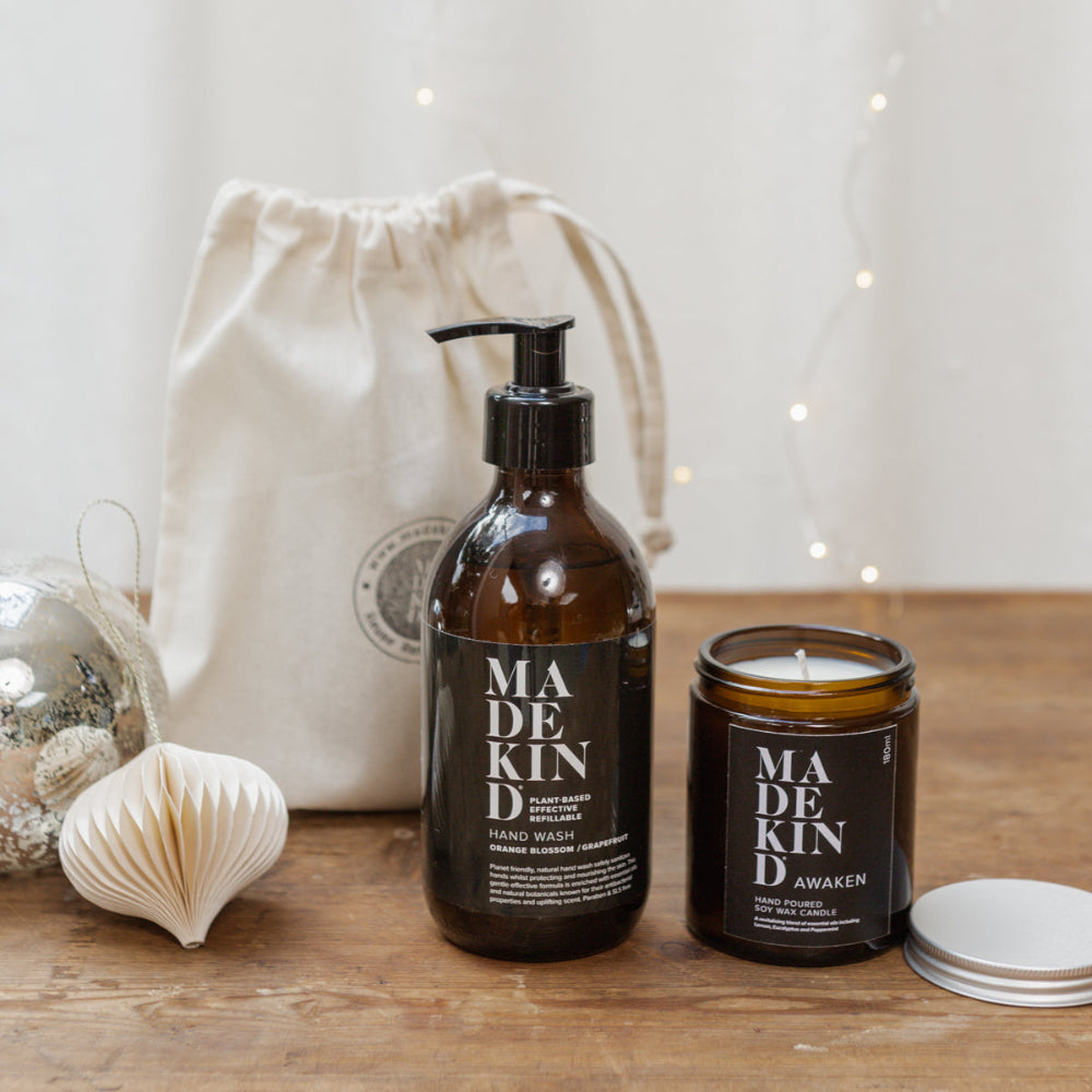 Bottle of 'MADEKIND' hand wash and candle on a wooden surface with a drawstring bag in the background.