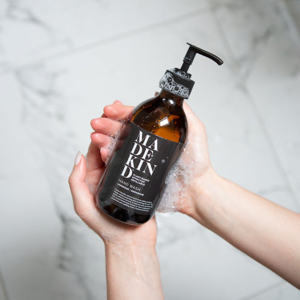 Person holding a bottle of Madkind hand wash with a pump against a neutral background