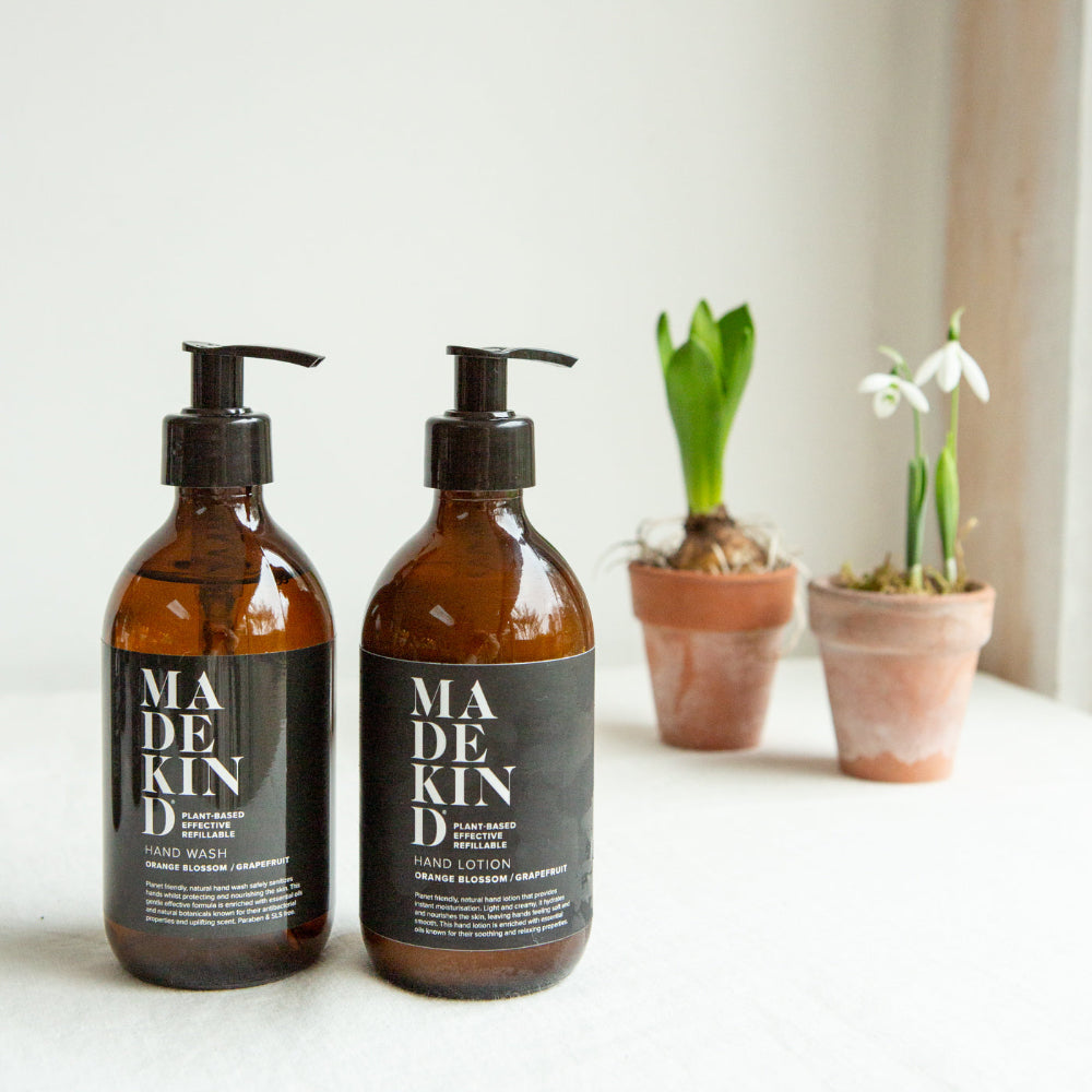 Two bottles of Made Kind hand wash and lotion on a white surface with plants in the background.
