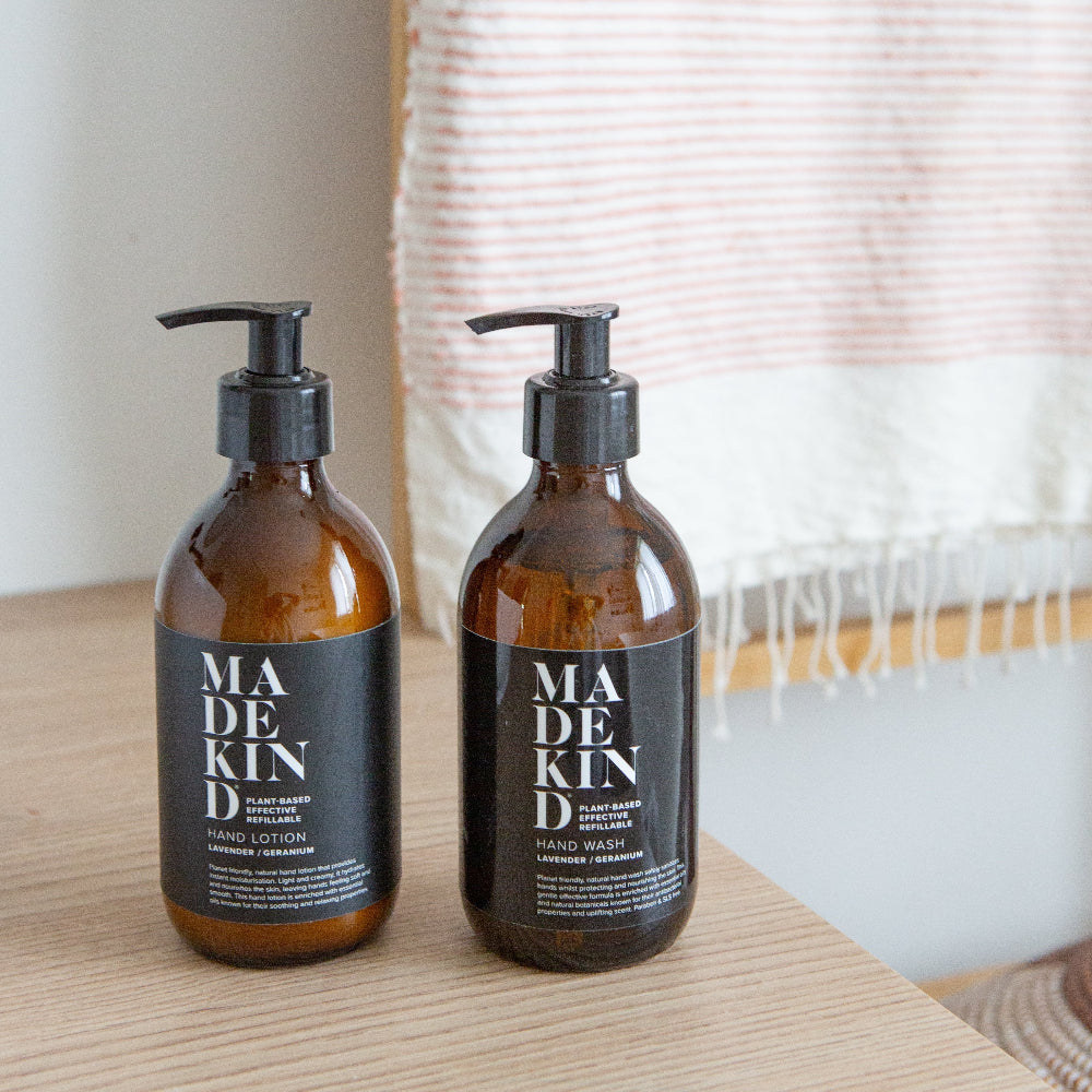Two bottles of Madekind hand wash and lotion on a wooden surface with a blurred background.