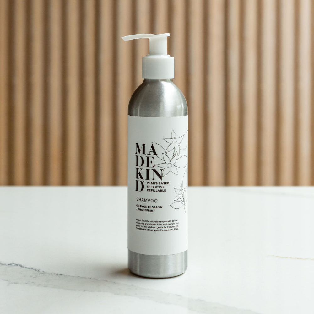 Shampoo bottle with 'MADEKIND' label on a marble surface with wooden background