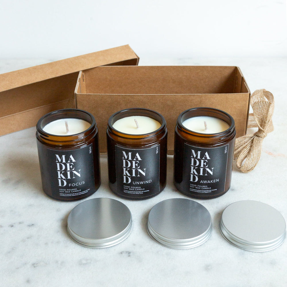 Three candles in glass jars with labels 'Focus', 'Unwind', and 'Awaken' on a marble surface with a cardboard box.