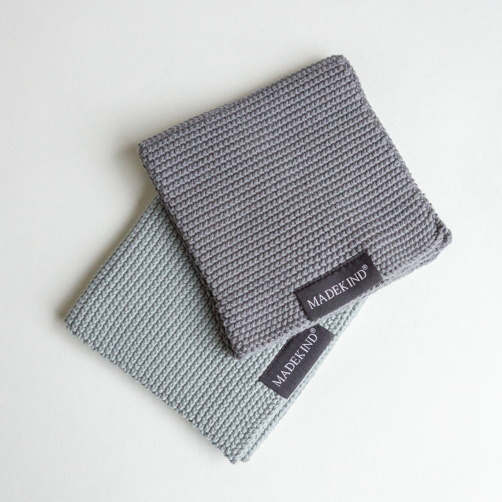 Two Charcoal grey organic knitted dish cloths with 'MADEKIND' label on a light background