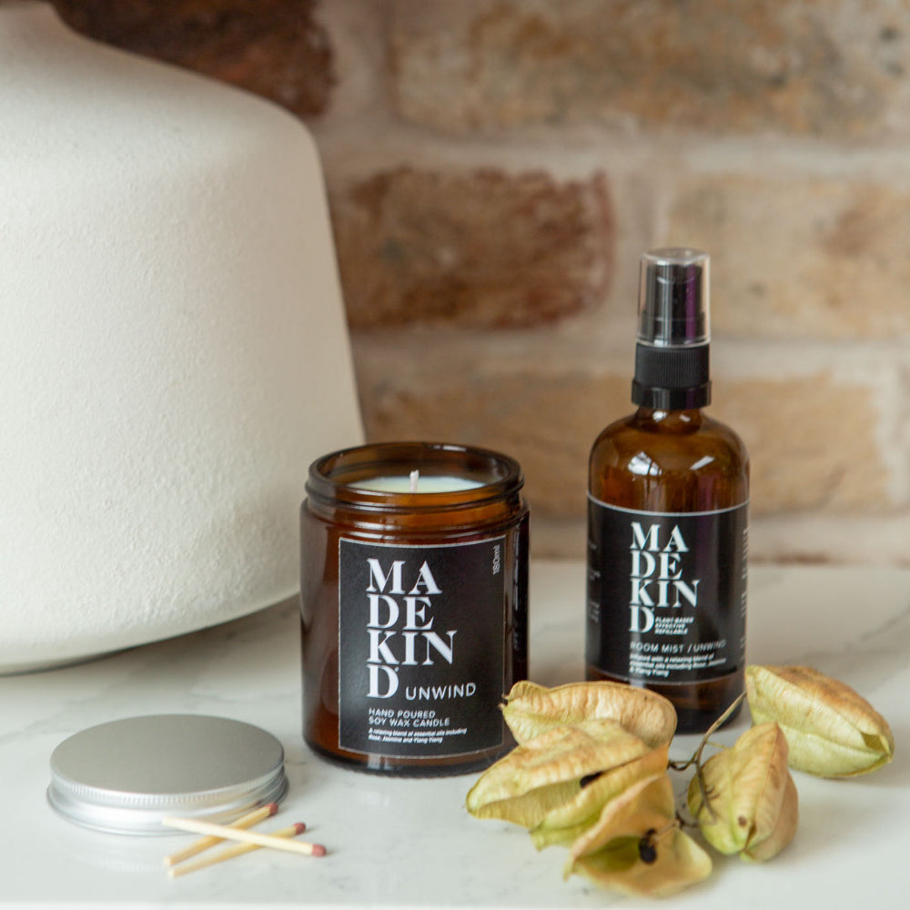 One brown bottle labelled 'MADEKIND' with matching candle on a surface with decorative elements.