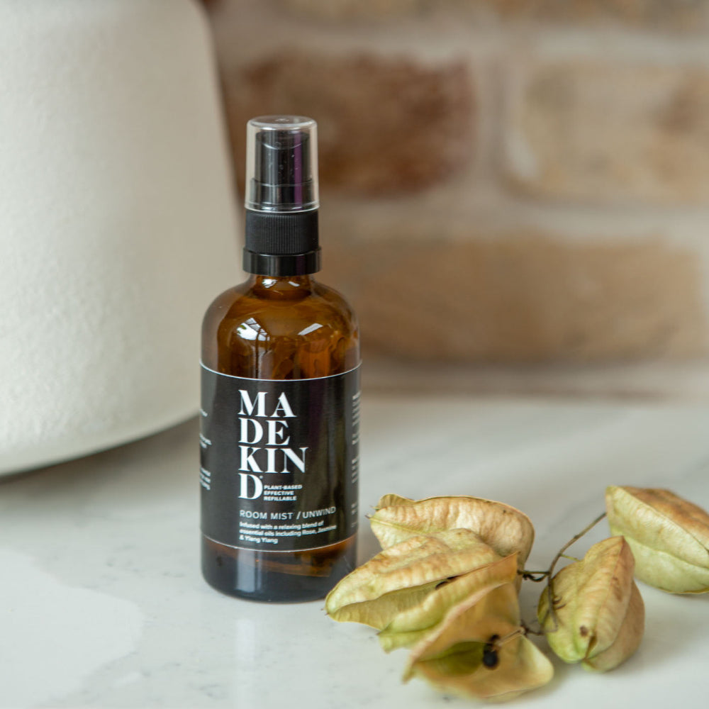 Brown spray bottle labelled 'MADEKIND' Room mist on a marble surface with decorative elements.