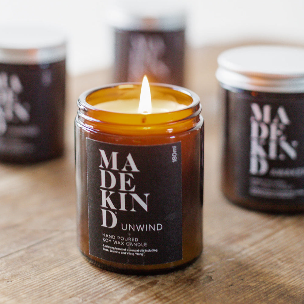Madekind candle labeled 'Unwind' on a wooden surface with other candles in the background.