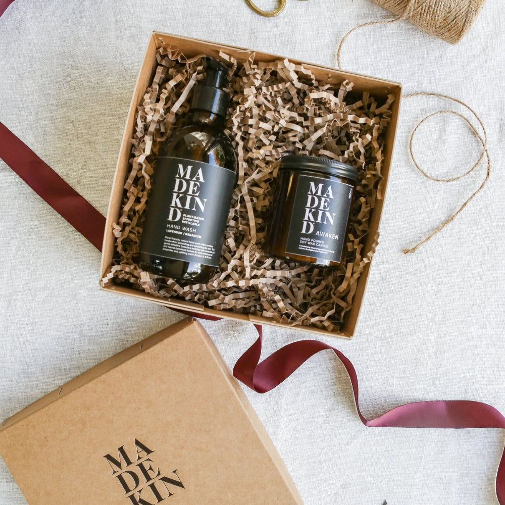 A bottle of Madekind hand wash with Awaken Candle in a gift box with ribbons on a light background
