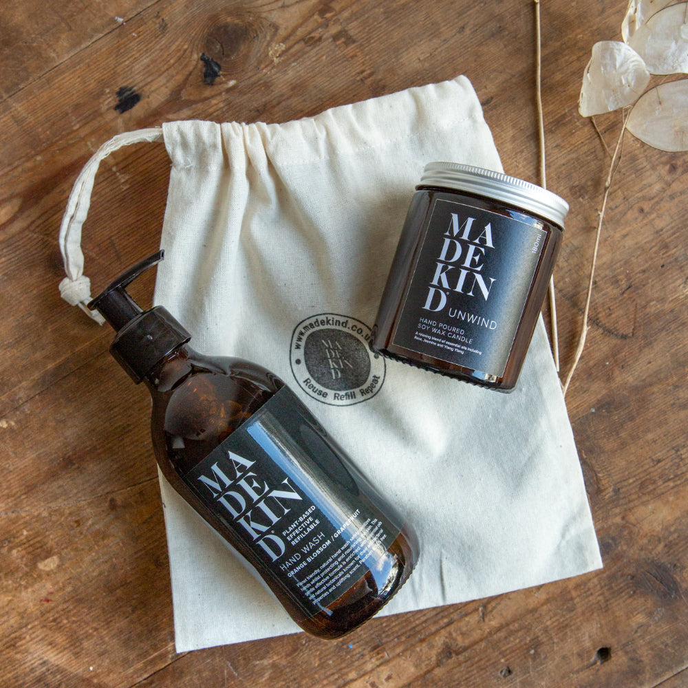 Two brown bottles with 'MADEKIND' branding on a wooden surface with a white drawstring bag.