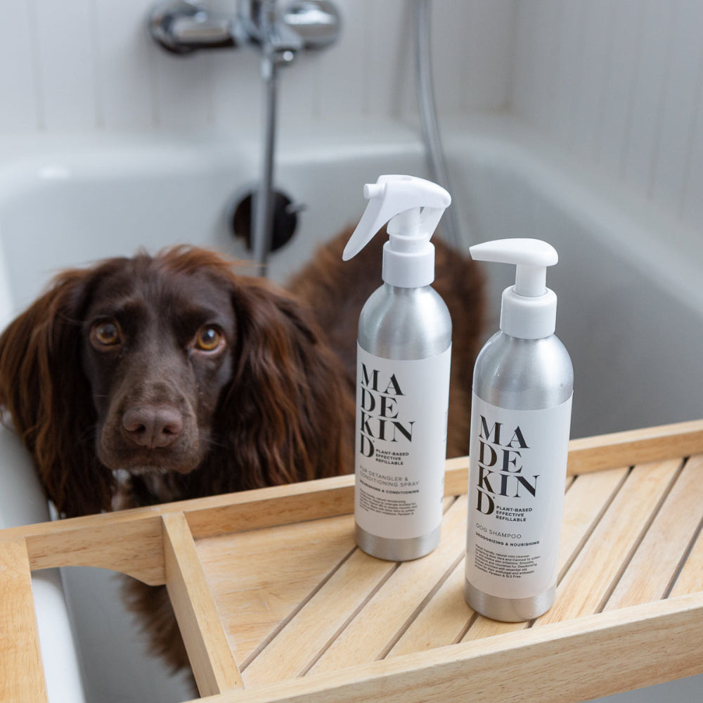 Two bottles of 'MADE KIND' dog shampoo and detangler products on a wooden tray with a dog in the background.
