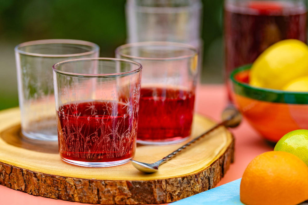 Two glasses of red juice on a wooden tray with fruits in the background