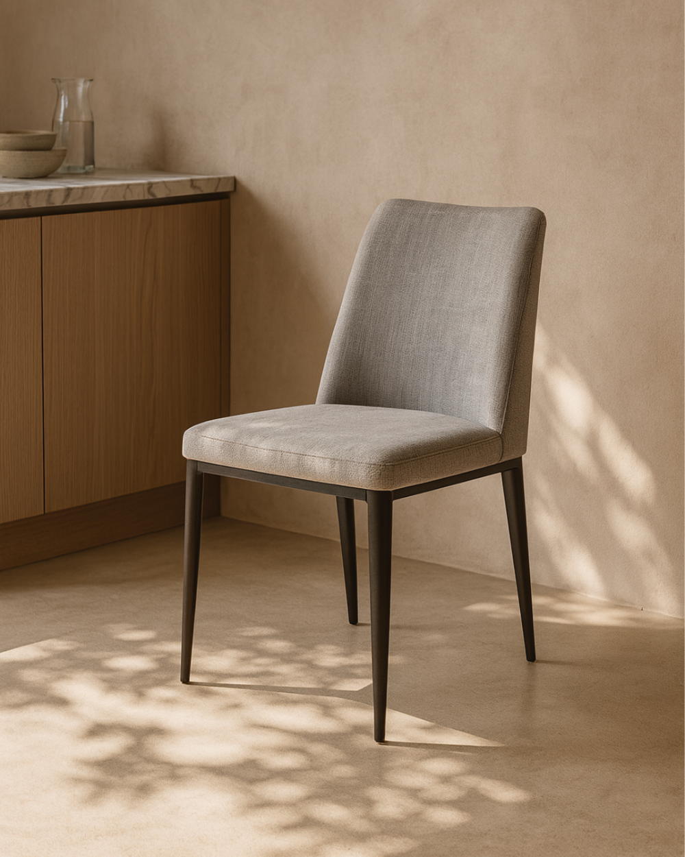 Medici Grey upholstered chair in a room with wooden cabinets and a neutral wall.