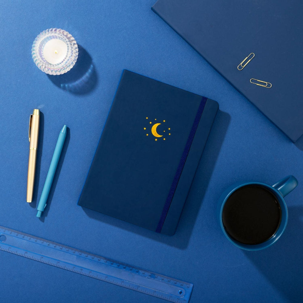 Midnight Blue Yop and Tom notebook with a debossed moon design on a blue surface with stationery items.