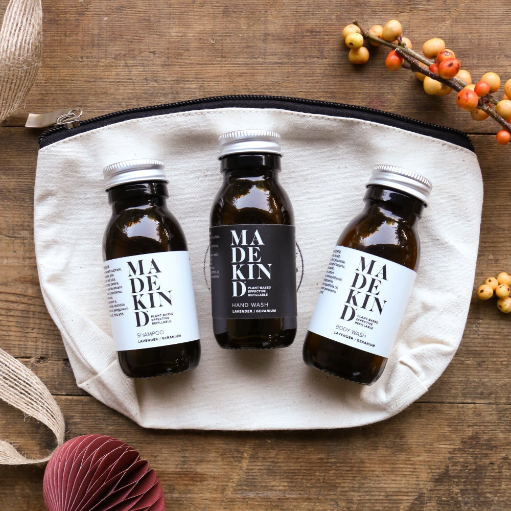 Three bottles of Madekind products on a beige pouch with decorative christmas elements on a wooden surface.